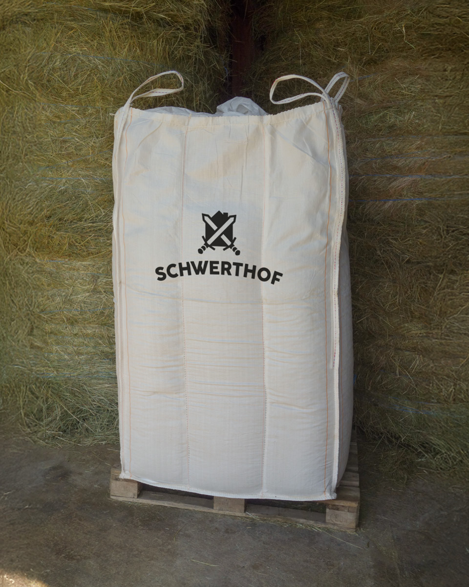 Eine Big Bag mit dem Schwerthof Logo auf einer Palette vor Heuballen.